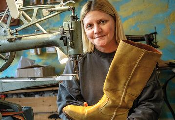 Schuhmacherin Karina Ranft in ihrer Werkstatt, sie hält einen gelben Stiefel in der Hand