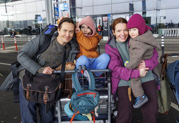 Vater, Mutter und zwei Kinder mit Kofferwagen und Gepäck an einem Flughafen
