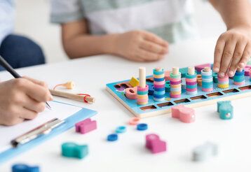Buntes Holzspielzeug für Kinder, die Hände eines Kindes spielen damit, Ergotherapeutin macht sich Notizen