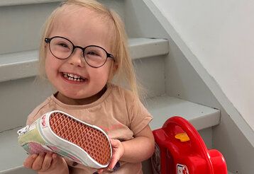 kleines Mädchen mit Down-Syndrom sitzt auf einer Treppe und hält einen Turnschuh in der Hand