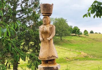 Holzskulptur einer Frau mit einem Korb auf dem Kopf in Landschaft