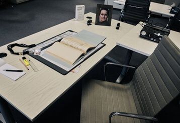 Schreibtisch in einem Bürozimmer, graue Stimmung, Bild mit Frauenporträt auf dem Tisch