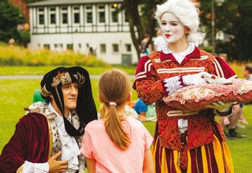 zwei märchenhaft verkleidete Schauspieler stehen mit einem Kind in einem Park