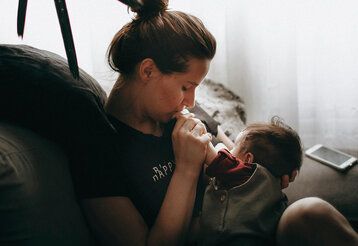 eine Mutter sitzt mit ihrem Baby auf einem Sofaund küsst dessen Händchen