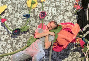 Ein Mann lehnt mit geschlossenen Augen an übergroßen Blumen.