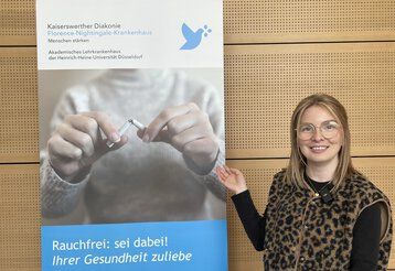 Frau lächelt in Kamera und deutet auf Plakat