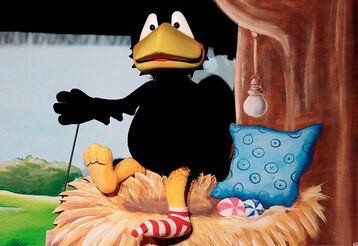 Die Puppe des kleinen Rabe Socke sitzte auf einem Nest mit Kissen.