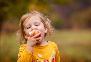 Kleines Mädchen isst leckeren roten Apfel