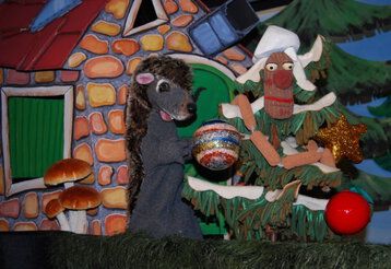 Eine Handpuppe in Form eines Igels steht vor einer weihnachtlichen Bühnenkulisse 