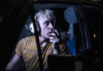 Ein Mann mit Kopfhörern sitzt im Dunkeln in seinem Auto und spricht in ein Funkgerät.