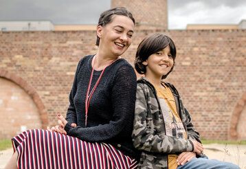 Mutter und Sohn sitzen vor altem Industriegebäude