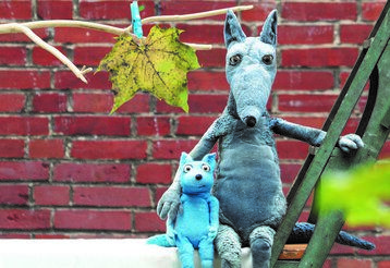 Der große Wolf und der kleine Wolf sitzen Arm in Arm vor einer Backsteinmauer.