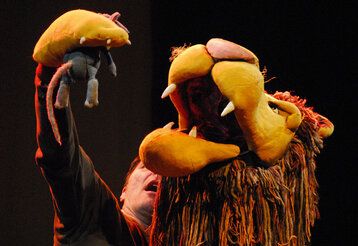 Eine Löwenpuppe des Figurentheaters Fithe hält in seiner Pranke eine Maus über sein geöffnetes Maul.