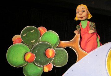 Die Goldmarie steht auf einer Puppenbühne vor dem Apfelbaum.