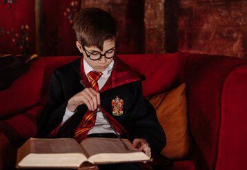 Ein als Harry Potter verkleideter Junge sitzt auf einem roten Sofa und liest.