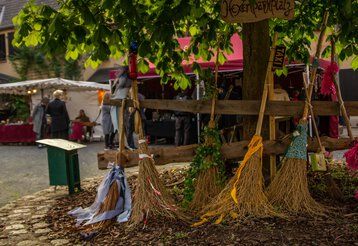 Vier Hexenbesen stehen an einen Baum gelehnt auf dem Hexenmarkt auf Burg Satzvey.