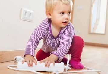 Baby girl playing with electrical extension  on floor at home