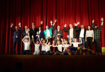 Jury und Preisträger der Kinderfilmtage im Ruhrgebiet von 2022 stehen auf der Bühne und winken in die Kamera.