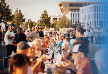 Lange Tafel auf der Strasse mit vielen Menschen die gemeinsam essen, trinken und sich unterhalten 