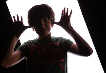 Ein Junge vor einer Lichtwand schaut feixend in die Kamera.