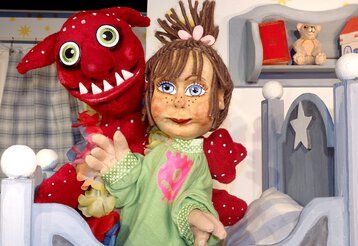 Zwei Handpuppen, ein Mädchen und sein Monster, sitzen auf einem Bett