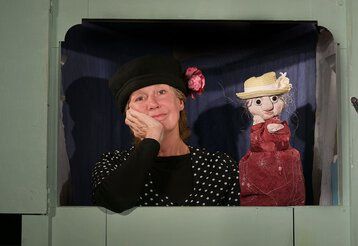 EIne Frau sitzt mit einer Handpuppe hinter einem Puppentheater