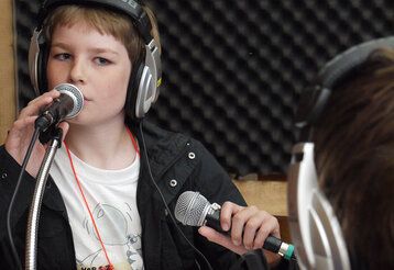 Ein Junge mit Kopfhörern in einem Tonstudio spricht ins Mikrofon.