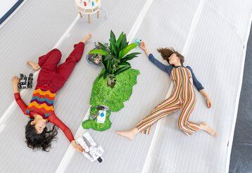 Zwei Tänzerinnen des Studio Sucrow liegen auf einer Bühne mit einer Pflanze in der Mitte