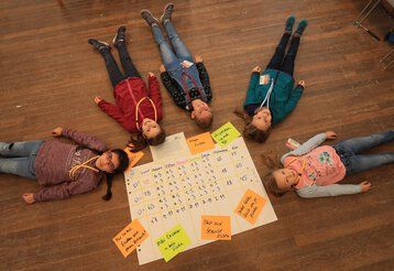 Fünf Mädchen liegen im Rahmen eines Workshops rund um einen Flipchartbogen auf dem Boden.