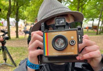 Ein als Detektiv verkleideter Junge fotografiert mit einer Polaroid Kamera im Park.