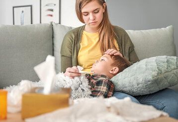 Woman measuring temperature of her sick son at home