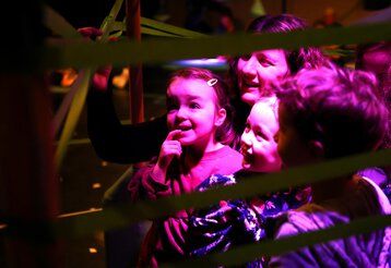 Drei kleine Kinder stehen mit ihrer Mutter staunend in einem Gewirr von Klebestreifen, die sich durch den Raum ziehen