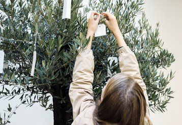 Ein Mädchen bindet ein kleines Schild an einen Zierbaum.