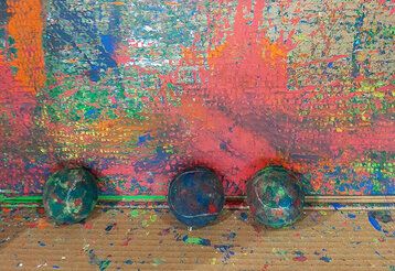 Drei in Farbe getränkte Tennisbälle liegen vor einer bun bemalten Wand.