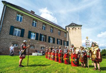 Männer in römischen Rüstungen stehen auf einer Wiese vor haus Bürgel