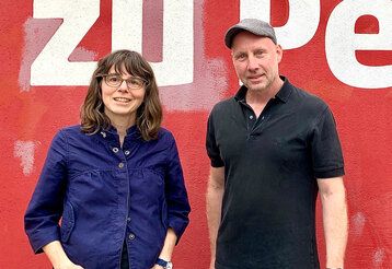 Porträt von Alexandra Wehrmann Sven Andre Dreyer vor einer roten Wand mit weißen Buchstaben