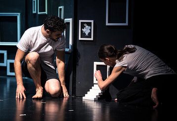 Mann und Frau auf schwarzer Bühne spielen an kleiner Treppe