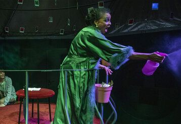 Eine Schauspielerin sprüht mit einer Sprühflasche herum, dunkle Stimmung