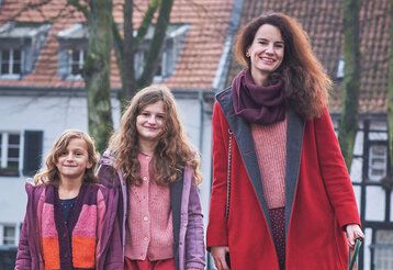 Anna Vogel mit ihren beiden Töchtern in Gerresheim, im Hintergrund ein Haus und ein Fachwerkhaus und kahle Bäume