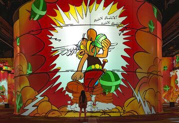 Asterix und Obelix immersive Ausstellung, Projektion von Asterix auf eine Säule, eine Frau steht klein davor