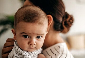 Baby ist bei der Mutter auf dem Arm und guckt kritisch in die Kamera
