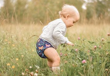 Baby mit Stoffwindel steht auf Blumenwiese