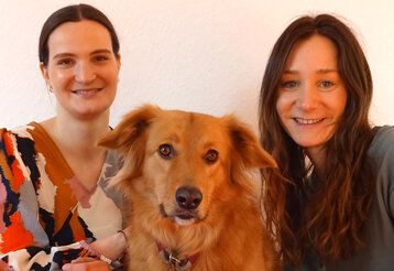 Porträt von zwei Frauen und einem Hund, im Hintergrund Raufasertapete