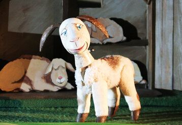 Puppentheater, eine Figur in Form eines Schafes steht auf der Bühne, im Hintergrund liegt ein schlafenden Schaf