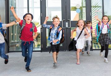 Grundschulkinder laufen jubelnd aus dem Schulgebäude