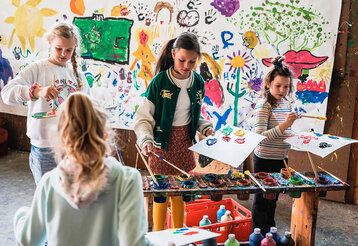 Vier Kinder malen an einem gemeinsamen Bild an einer Wand