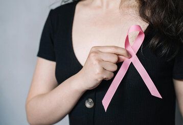 eine Frau hält sich eine rosa Schleife vor den Oberkörper