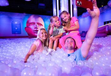 Vater, Mutter und zwei Töchter in einem Bällebad im Bubble Planet