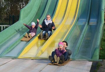 Vater, Mutter und zwei Kinder rutschen auf der Rutschbahn des Bubenheimer Spielelandes
