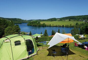 Zeltplatz mit mehreren Zelten an einem Seeufer, Wald und Wiese, im Sommer